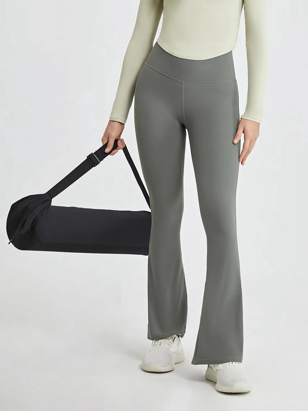 Woman wearing high-waisted flare pants for yoga, holding a sports bag, showcasing durable nylon-spandex blend for intense activities.